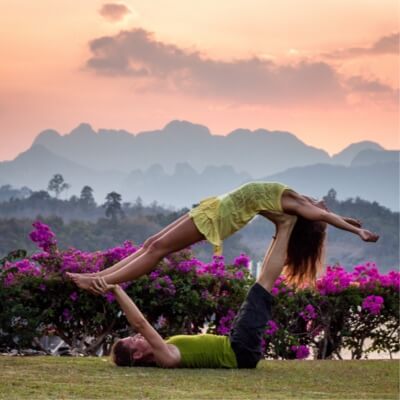 man and woman doing yoga pose outside with flowers and mountains in the background