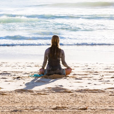 back view of woman doing cross legged yoga pose on the beach